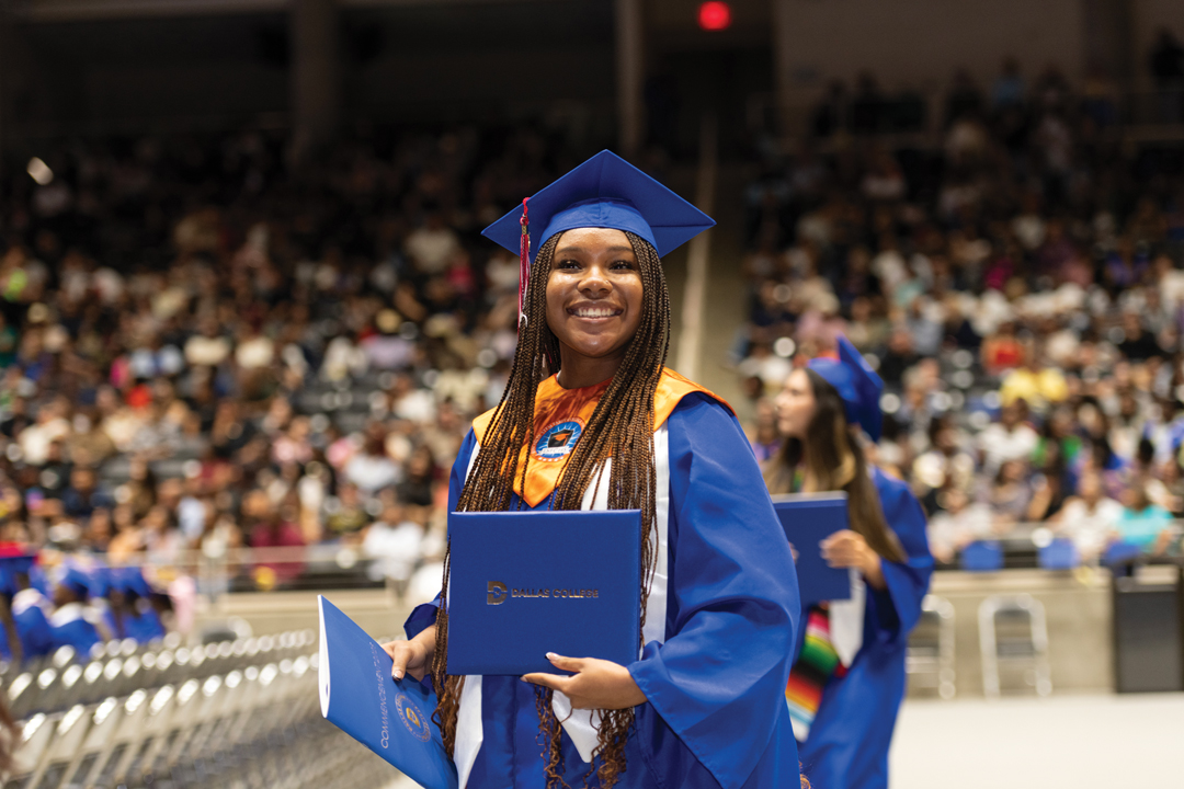 Dallas College female graduate holding diploma proudly in front of crowd