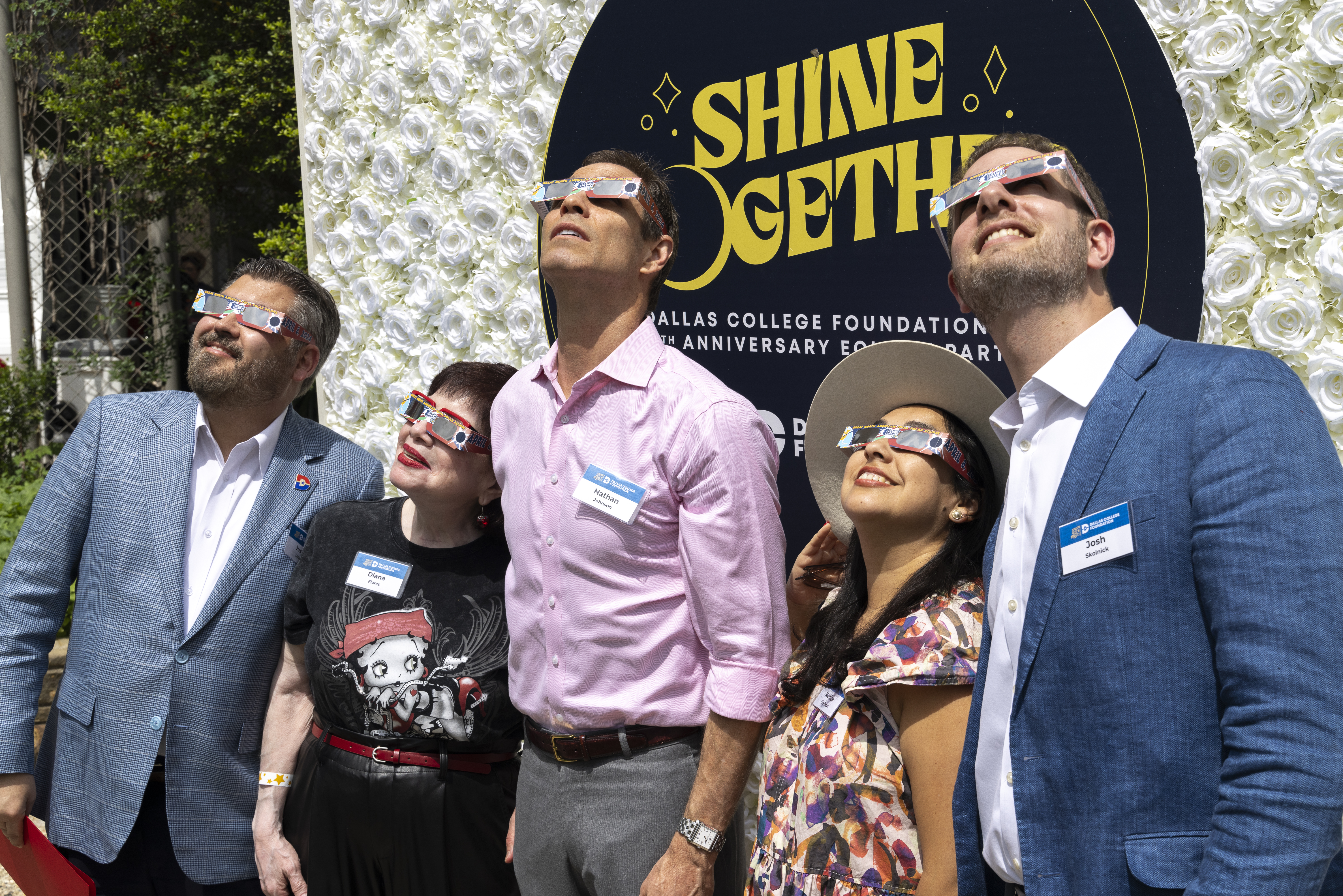 A group of eclipse viewers and Dallas College Foundation leadership and board members view an eclipse together with glasses protecting their eyes